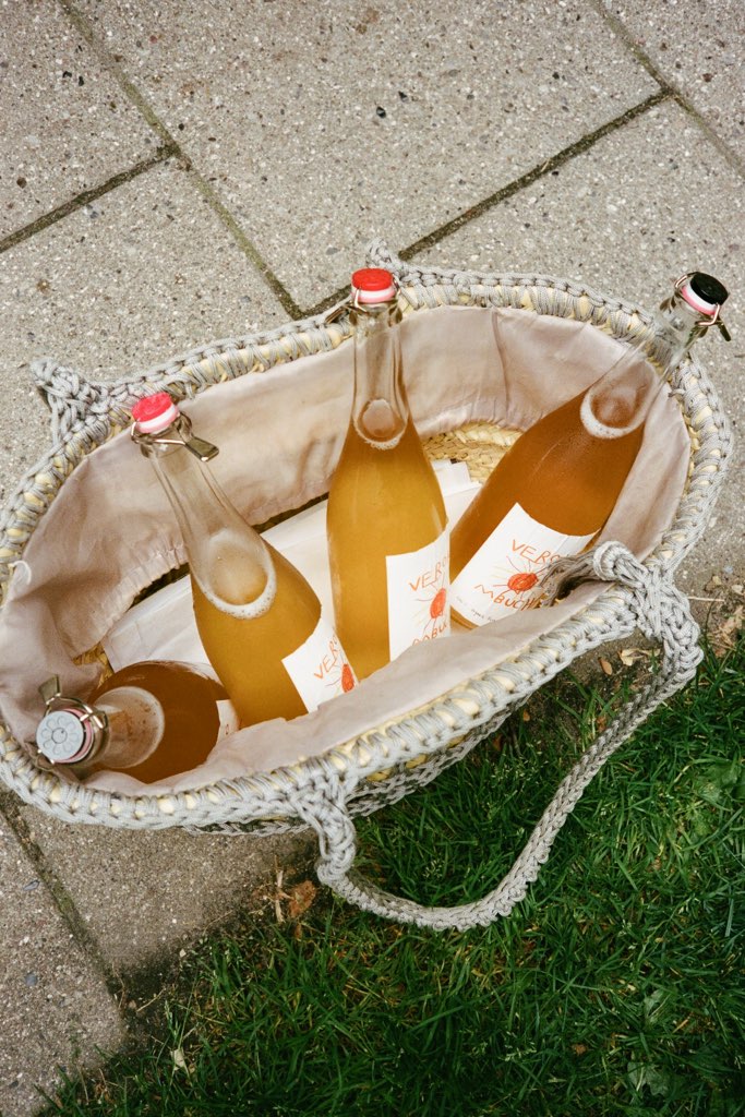 Four bottles of Verokombucha in a woven basket on the pavement.