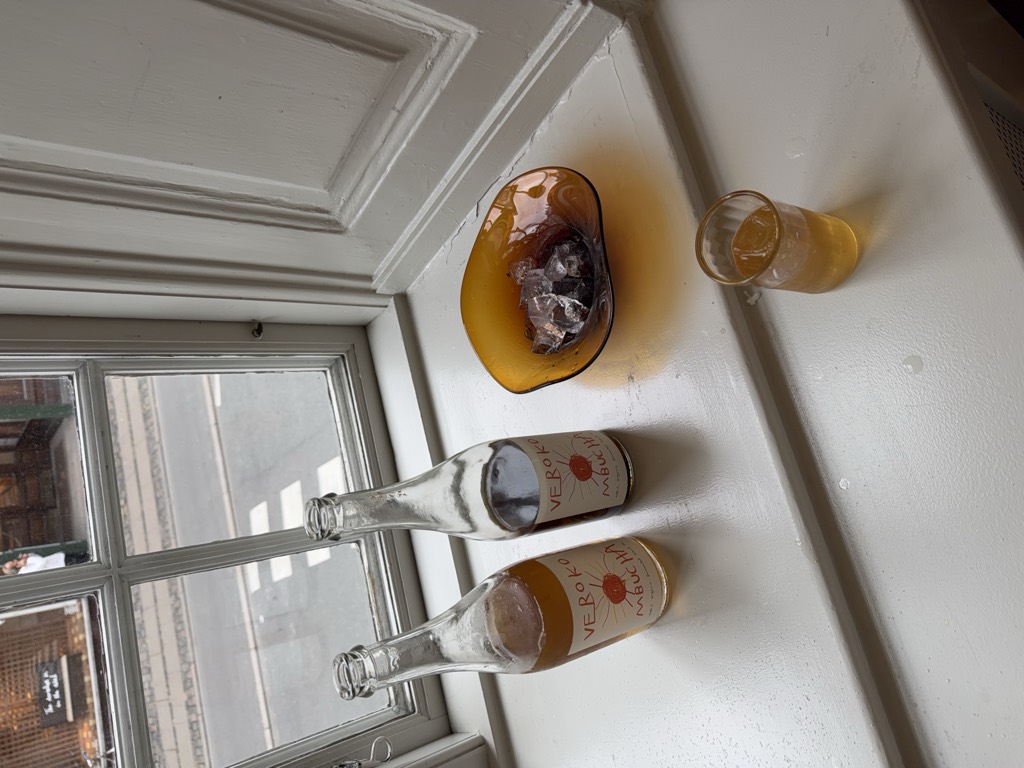 Two bottles of Verokombucha and a glass on a white windowsill.